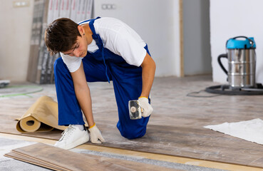 Young male repairer installing laminate flooring in apartment