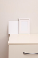 Mockup of a white empty photo frame and card standing on a dresser