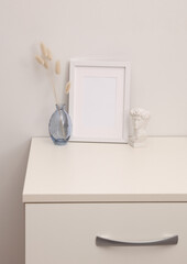Mockup of a white empty photo frame and decor standing on a dresser