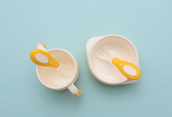 Bowls with spoon and fork on blue pastel background. Accessories for feeding small children. Top view