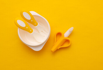 Bowl with spoon and fork on yellow background. Accessories for feeding small children. Top view