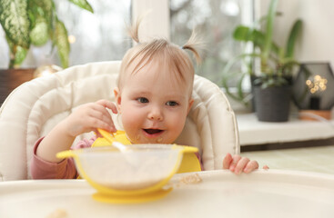 Cute little baby girl eats on her own at the feeding table