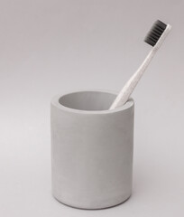 Plastic toothbrush in concrete cup on grey background. Personal hygiene, beauty concept
