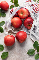 Fresh red apples spilling from reusable mesh bag on table