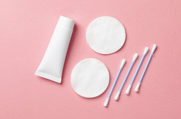 Cream tube with cotton pads and ear buds on a pink background