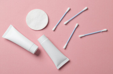 Cream tubes with cotton pads and ear buds on a pink background