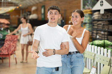 Positive friendly young adult couple, guy and girl, looking with interest for comfortable furniture...