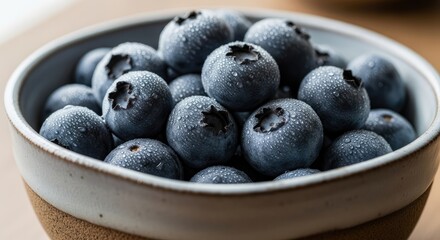Close-up of fresh, ripe blueberries covered in water droplets in a ceramic bowl, showcasing healthy and organic fruit.