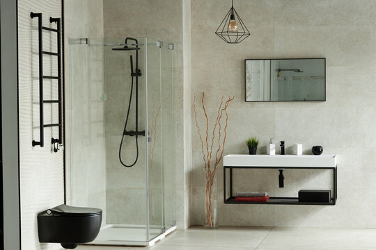 Modern bathroom interior featuring glass shower enclosure, wall mounted black toilet, rectangular mirror, minimalist sink with accessories, decorative branches, tiled walls