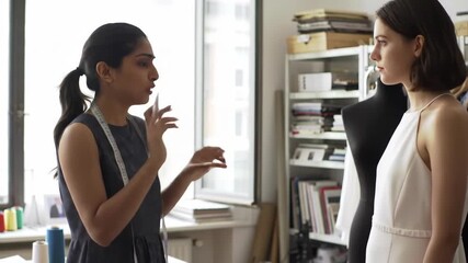 Two women, diverse group, in fashion design studio with mannequin, discussing dressmaking, designer with tape measure, dress, creative process, teamwork, studio, daytime.