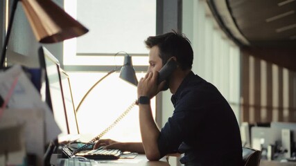 Focused businessman talking on landline phone at office desk - Powered by Adobe