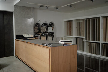 Obraz premium Empty showroom counter displaying sample books and material swatches with shelving units holding various tile and flooring samples in modern commercial interior setting