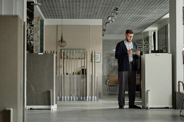 Middle aged Caucasian man standing in modern showroom using digital tablet, examining large display...