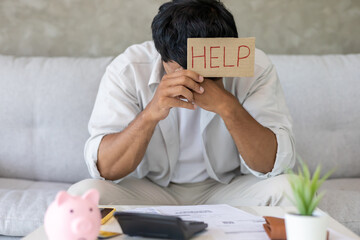 Stressed and headache asian man with large bills or invoices no money to pay to expenses and credit...