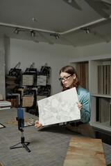 Caucasian young adult woman presenting large marble tile sample while recording video on smartphone...