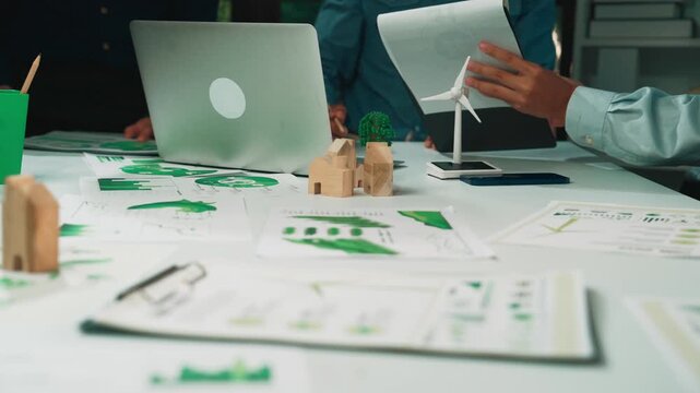 Professionals engage in a collaborative session, analyzing data and discussing sustainable solutions. A wind turbine model adds a creative touch to their innovative workspace. SACTR - Powered by Adobe