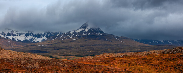 Panoramic view of scenic mountain landscape with dark cloud cover in Iceland countryside during...