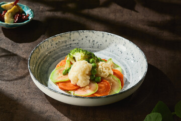 Steamed broccoli, zucchini, carrot and cauliflower in bright rustic lighting, overhead food composition