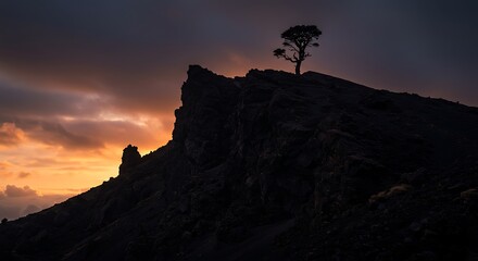 Obraz premium Dramatic silhouette of a solitary tree standing on a mountain ridge during a vibrant and colorful dusk