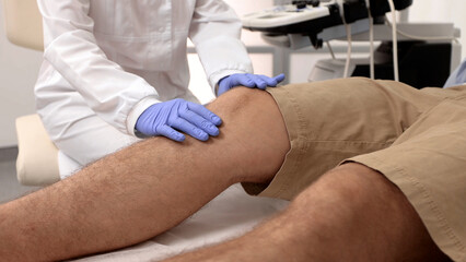 Treatment for knee injuries. Adult man with knee injury during consultation with doctor traumatologist at medical clinic. Ultrasound exam of knee