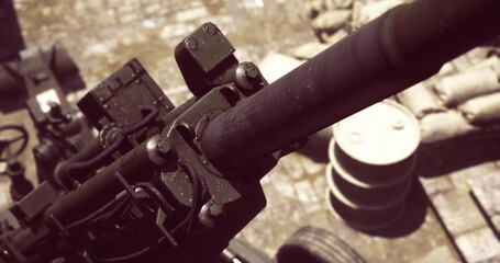A close view of artillery equipment shows intricate details of the barrel and mechanisms while surrounded by military supplies during outdoor training.