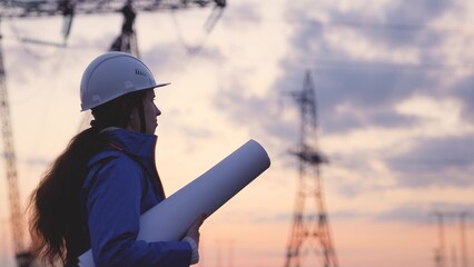 An electrician at a high voltage power plant works with a project at sunset in the sky, electrical...