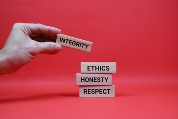 Hand Arranging Wooden Blocks with Ethics, Honesty, and Integrity Texts. Isolated on red background