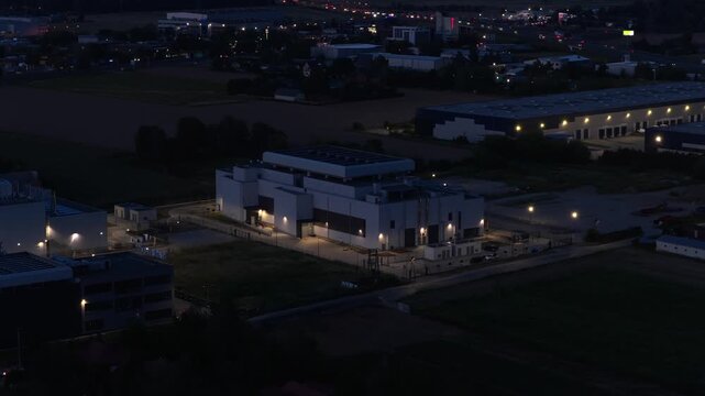 Aerial night view of a modern data center in Warsaw, Poland, surrounded by logistics hubs and industrial warehouses. Illuminated secure facility for servers, cloud storage, and digital networks