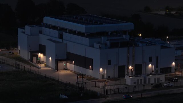 Aerial orbit at night over a modern data center facility in Warsaw, Poland. Illuminated secure building representing digital infrastructure, cloud storage, servers, and network technology