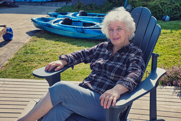 Senior woman relaxing in Adirondack chair near kayaks
