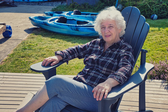 Senior woman relaxing in Adirondack chair near kayaks