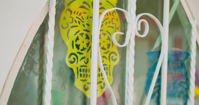 A yellow Dia de los Muertos skull papel picado decoration in a white tomb window. Mexico City.