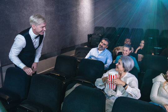 Smiling usher engaging with audience members enjoying popcorn and watching a movie in a cozy cinema atmosphere