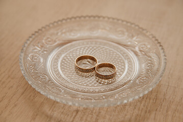 Golden wedding rings lie on a crystal platter on the table on the day of the wedding ceremony