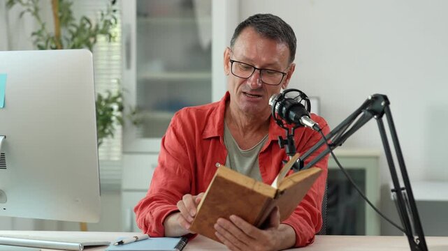 Middle-aged content creator reading his book aloud, recording his voice using a professional microphone, sitting at his desk in his home studio