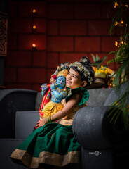 Little girl in cultural costume holding Krishna statue with love and devotion, South Indian...