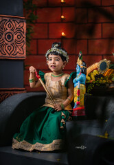 Obraz premium South Indian child dressed in ethnic costume celebrating Hindu festival with Lord Krishna doll, Happy Janmashtami background 2025, festival photography.