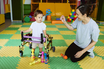 Professional physical therapist assists young boy patient as he uses a walker in a bright and supportive therapy environment
