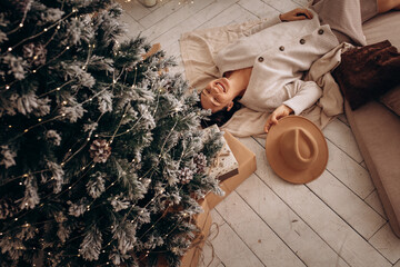 The model is a beautiful woman, happy at home at Christmas, lying under the tree