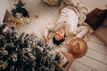 The model is a beautiful woman, happy at home at Christmas, lying under the tree