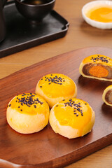 Traditional Asian egg yolk pastries with black sesame seeds and sweet bean paste filling on wooden serving board