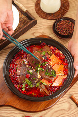 Spicy Chinese Hot Pot with Blood Sausage and Vegetables in Traditional Black Ceramic Bowl on Wooden Table