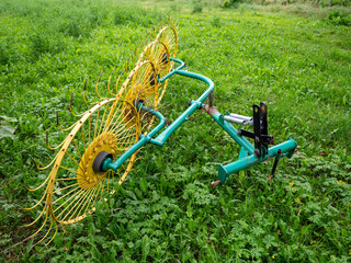 Yellow rotary rake wheels on grass, agricultural machine pulled by tractor for turning grass to dry for haymaking.