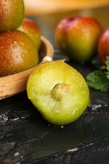 Fresh Ripe Mango Cut in Half Showing Juicy Yellow Flesh with Whole Mangoes in Wooden Bowl on Dark Slate