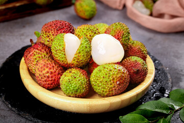 Fresh Hainan Lychee Fruits in Wooden Bowl with Exposed White Flesh on Dark Stone Background