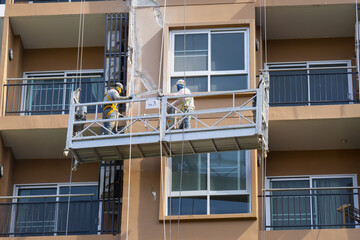 Construction workers on suspended platform repair building facade. Safety gear and teamwork are essential for high rise maintenance