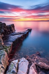 Fototapeta premium Dramatic Sunset Over Rocky Coastline With Calm Water