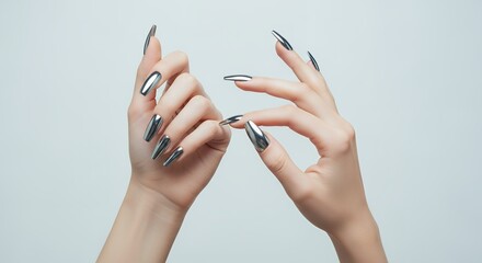 Two female hands with long sharp metallic silver coffin shaped fingernails elegantly posed against a plain light grey background manicure long nails coffin nails chrome nails fashion