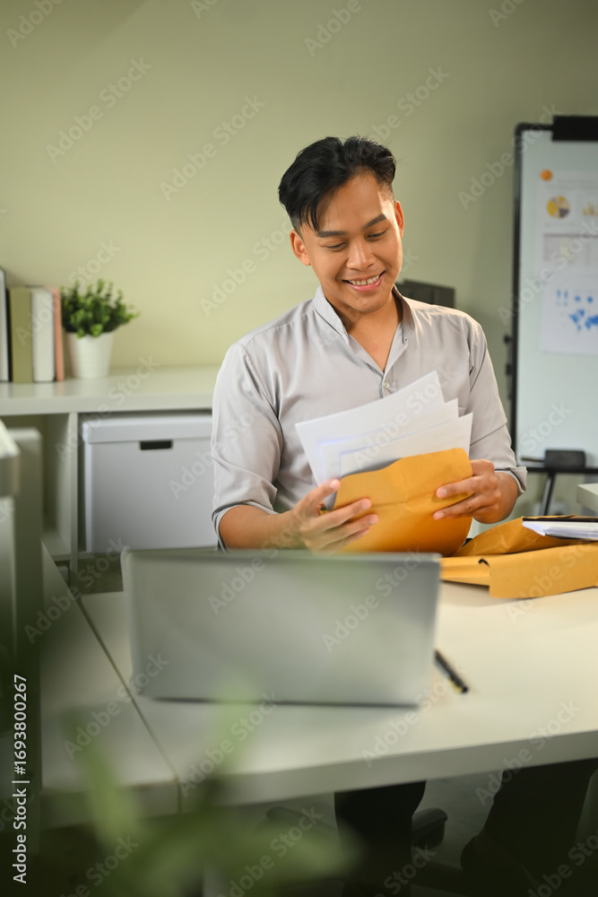 Poster smiling office worker organizing paperwork from a brown envelope at a modern desk