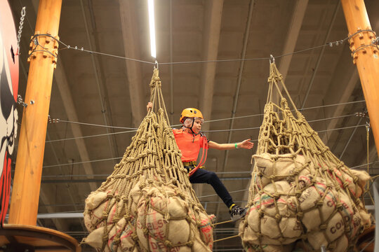 a child navigating a challenging rope course at a children's activity center. Dressed in protective gear, the young adventurer traverse the intricate pathways suspended high above the ground